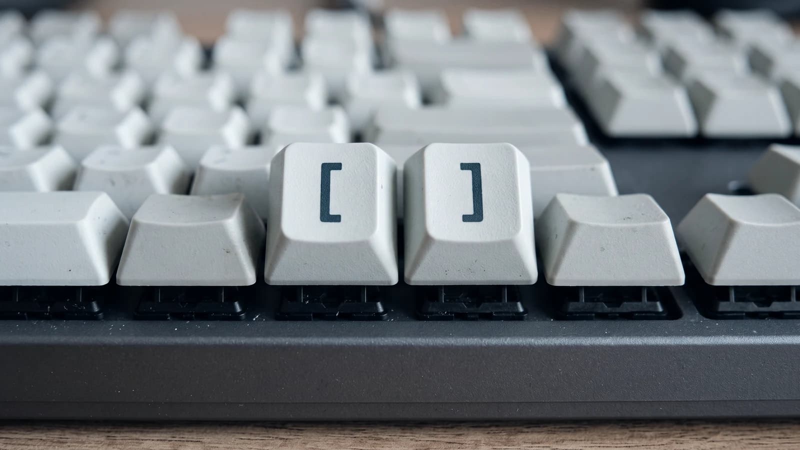 Two keys on a pale grey mechanical keyboard, printed with an opening and a closing square bracket, among rows of blank keys