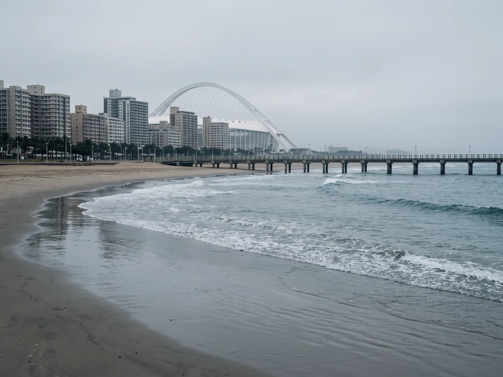 Durban's beachfront and a pier at low tide, with the arch of Moses Mabhida Stadium behind.